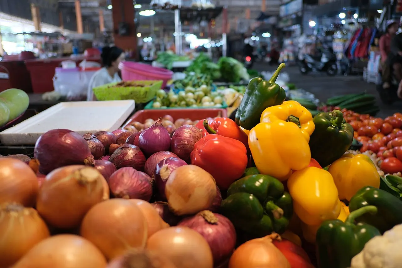 A colorful market stall piled with fresh peppers and onions.